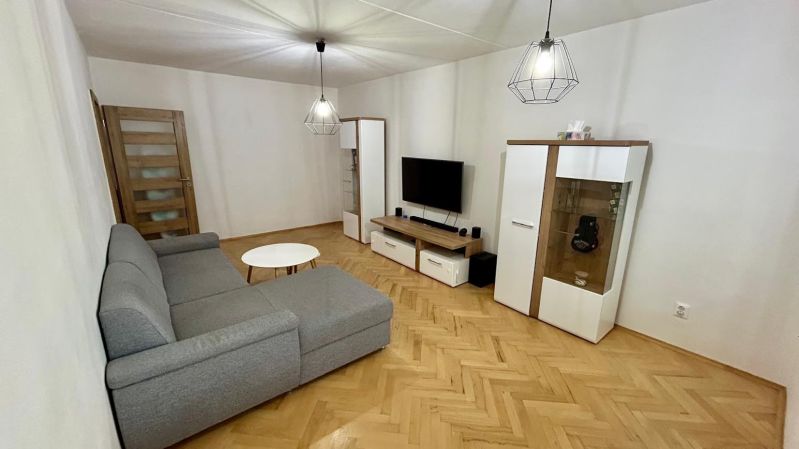 Living room with a sofa, television, and wood-patterned flooring in a 3-room apartment.