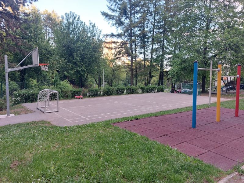 A playground with a basketball hoop and climbing frames in Banská Bystrica, surrounded by greenery.