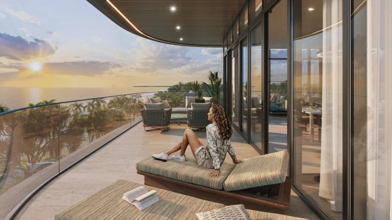 A woman is sitting on the terrace of a studio apartment with an ocean view at sunset.
