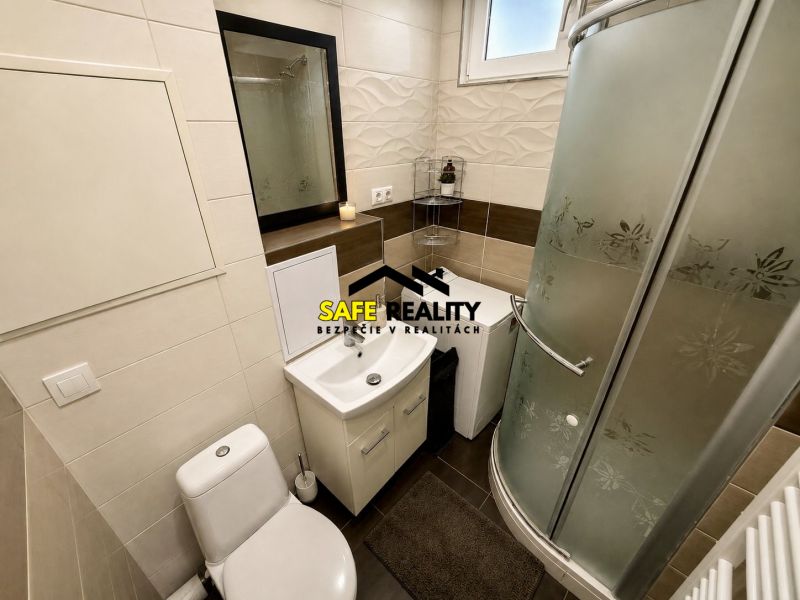 A bathroom in a studio apartment with a toilet, sink, and shower, white tiles on the walls.