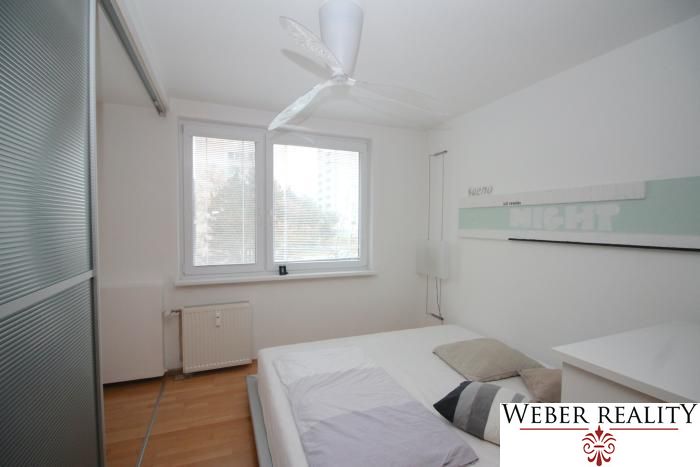 A bright bedroom with a large window and a wooden decor floor in a 3-room apartment.