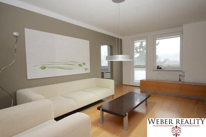 A bright living room in a three-room apartment with wood-patterned flooring and a large sofa.