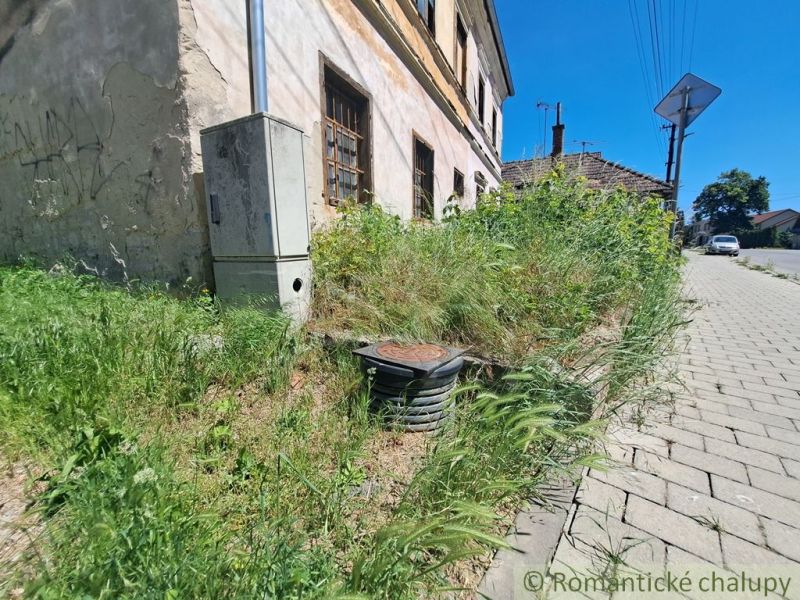 A neglected family house in Klátova Nová Ves surrounded by tall grass and a walkway.