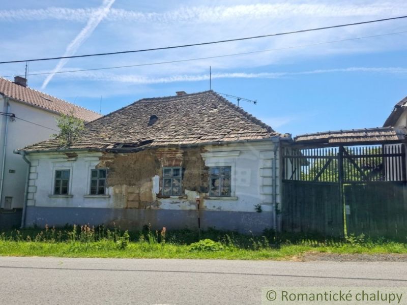 The old facade of a rural family house in Ozdín, surrounded by greenery and a fence.