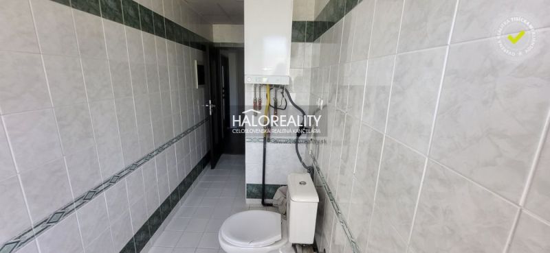 A bathroom with white tiles and a toilet in a 3-room apartment.