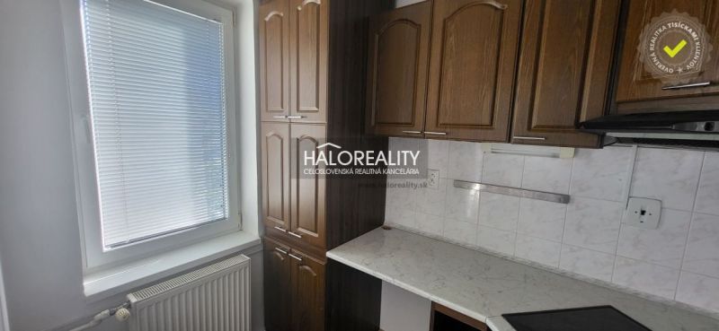 A kitchen with a window, brown cabinets, and a white countertop in a three-room apartment.