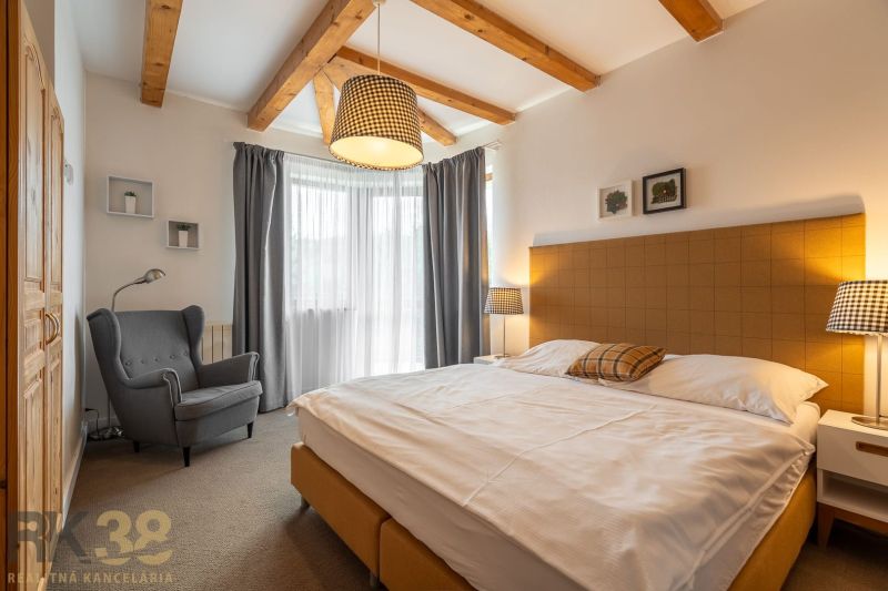 A bedroom in a 3-room apartment with wooden beams and a comfortable chair by the bed.