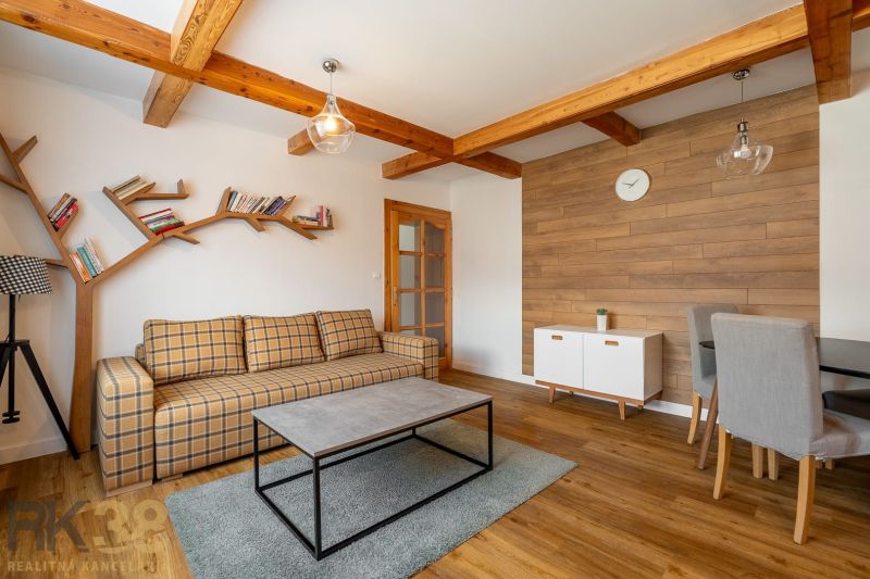 A bright living room in a three-room apartment with a wooden decor floor and wooden beams.