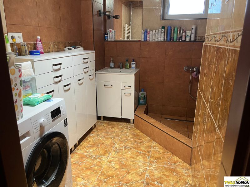 A bathroom with white cabinets, a washing machine, and a shower in a family house.