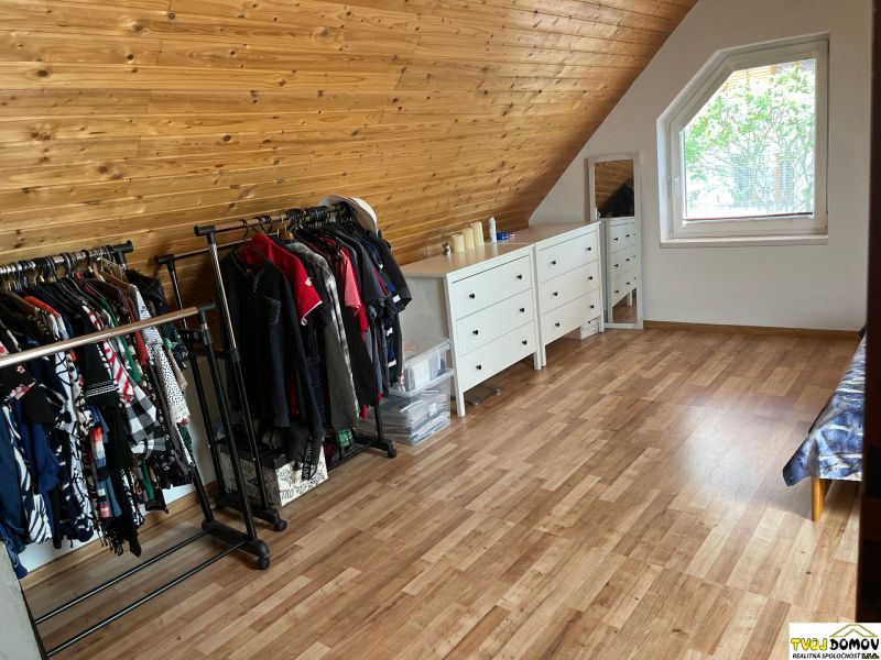 An attic room in a family house with clothing and a dresser, wooden decor flooring.