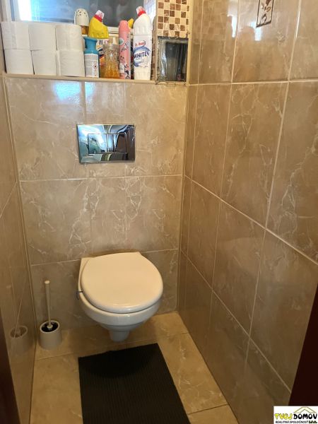 Toilet with tiles in a family house. Shelves with cleaning products and toilet paper.