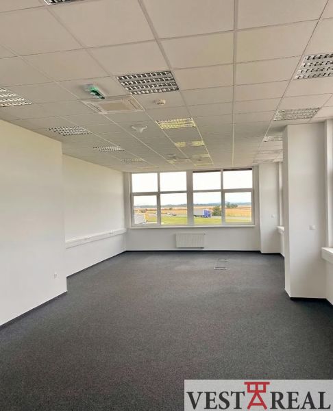 Office spaces with carpet flooring and a large window in a warehouse and hall building.