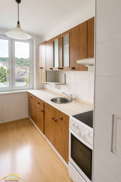 The kitchen of a 3-room apartment with a door to the balcony and a floor with a wooden decor.