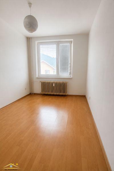 An empty room in a three-room apartment with a wooden patterned floor and a radiator.