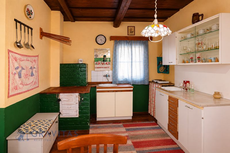 A kitchen in a cottage with traditional furnishings, a fabric curtain, and a floor with a wooden decor.