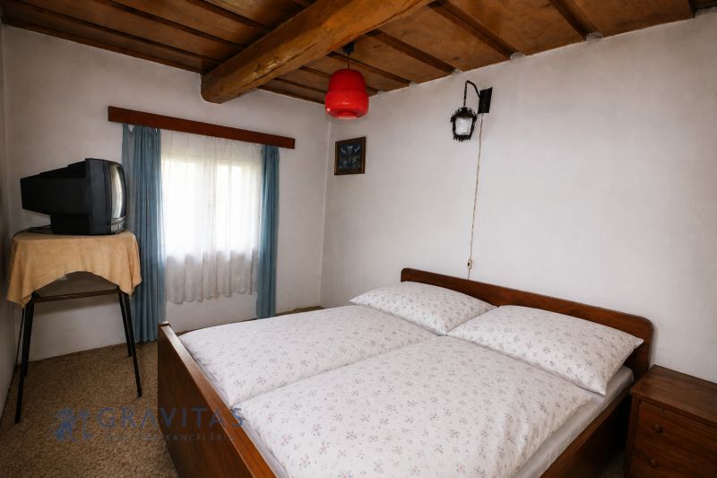A cottage with a cozy bedroom, wooden ceiling, and a retro TV on a table.