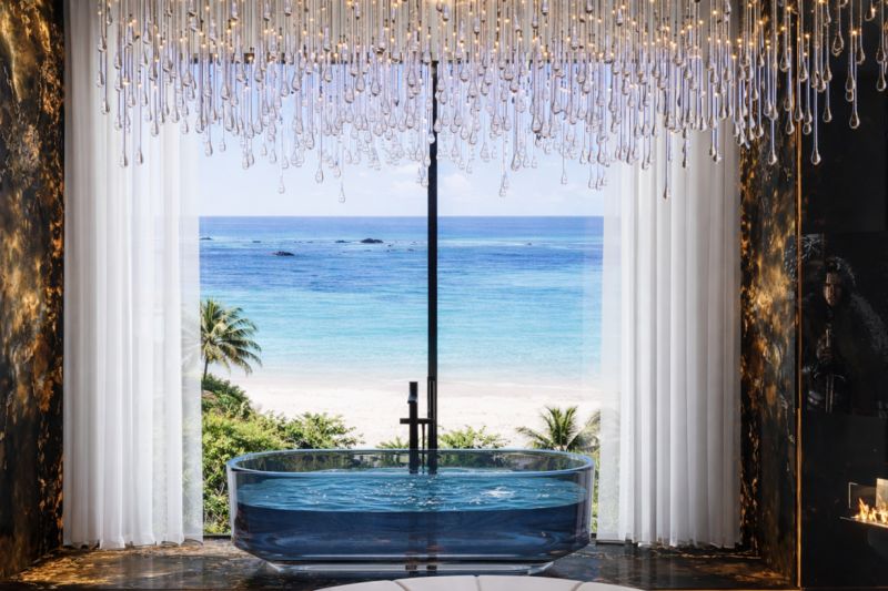 A glass bathtub with a view of the beach from a 5 or more room apartment.