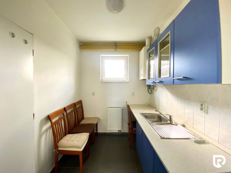 A kitchen space with blue cabinets and white tiles, three wooden chairs.