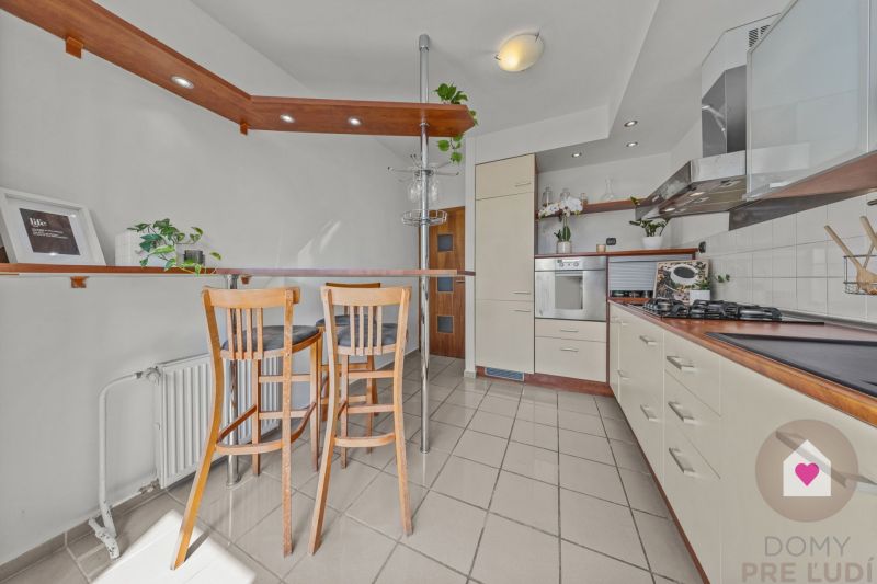 A kitchen in a 4-room apartment with a stove, a bar counter, and wooden chairs.