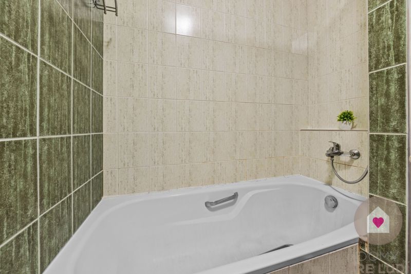In the bathroom of a 4-room apartment, the bathtub is surrounded by ceramic tiles with a plant.