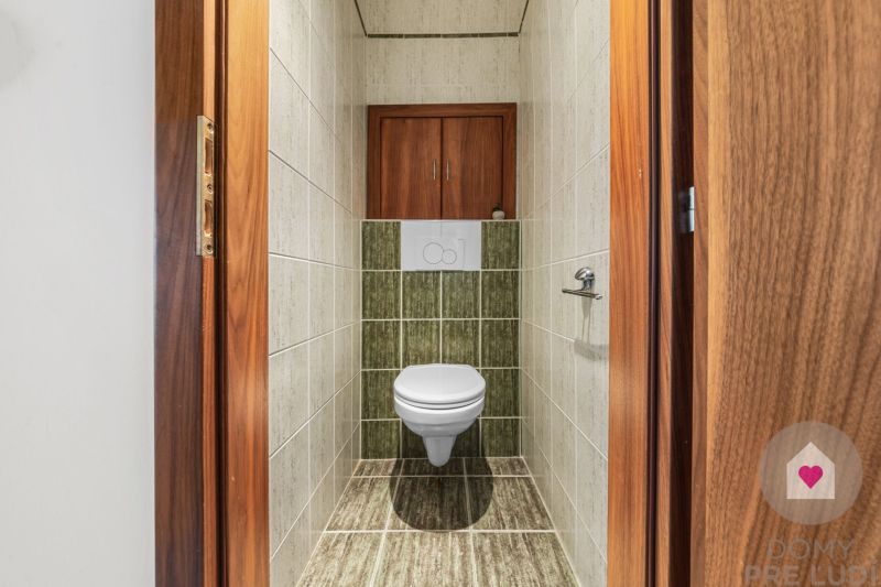 A toilet in a 4-room apartment with tiles, wooden decor on the door and floor.