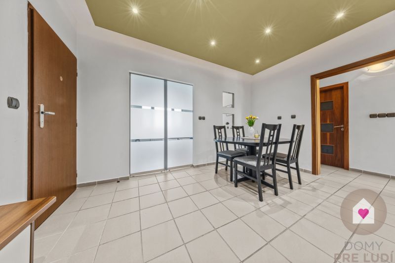 Dining table with chairs in a 4-room apartment with tiles and ceiling lights.