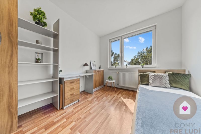 A room in a 4-room apartment with a wooden decor floor, a desk, and a bed.