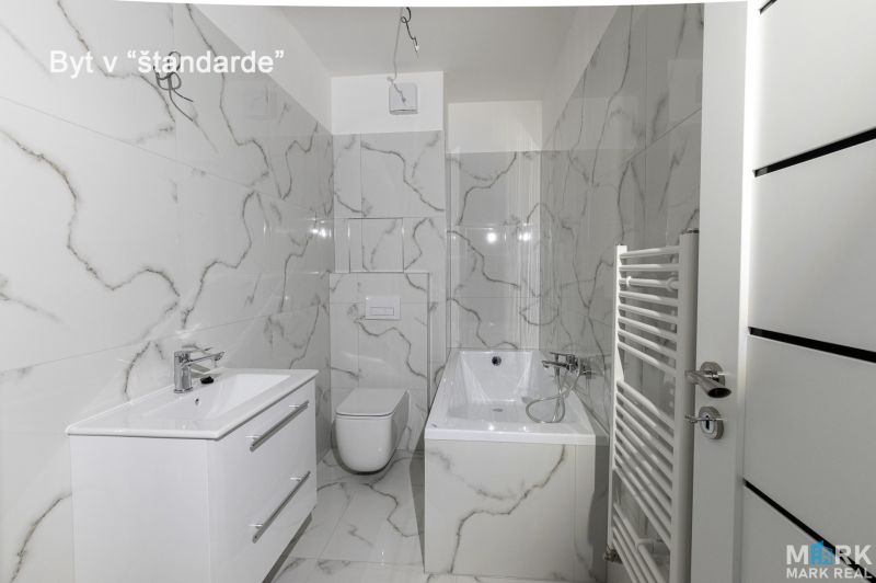 A bathroom with white tiles, a bathtub, and a sink in a 2-room apartment.