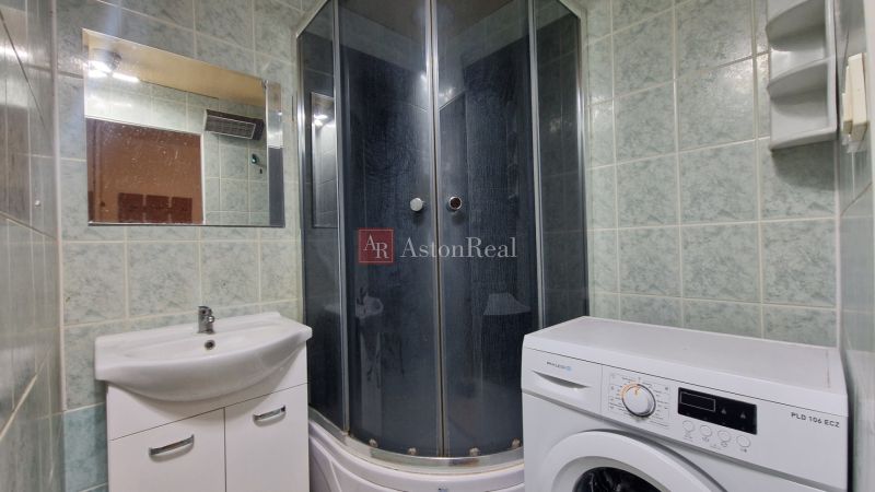 Bathroom with a washing machine and a shower in a 2-room apartment, green tiles and a mirror.