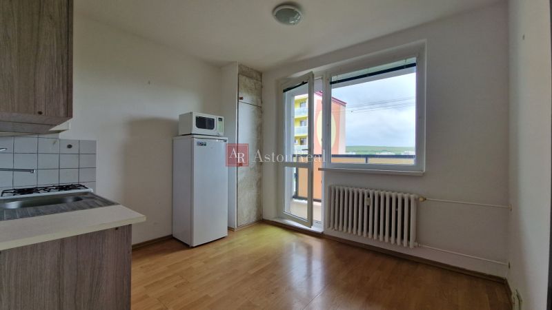 A kitchen in a 2-room apartment with a wooden decor floor, a refrigerator, and a view from the balcony.