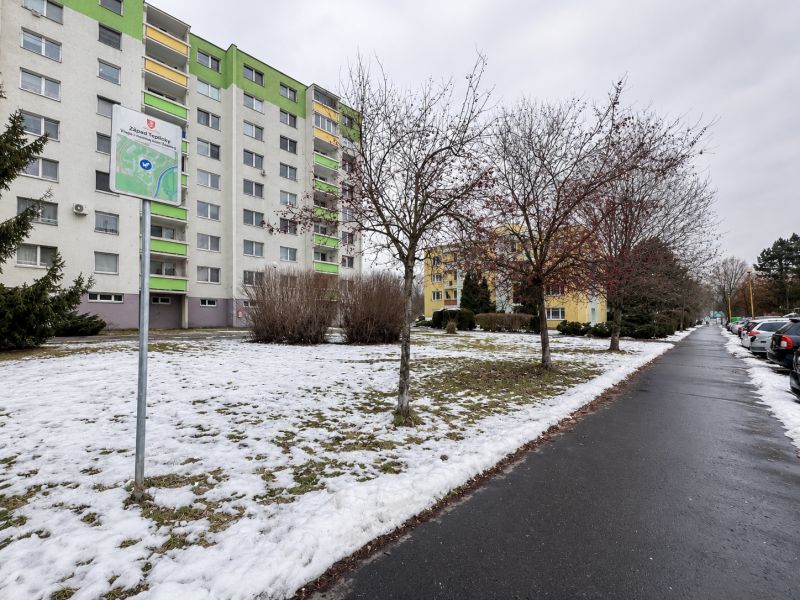 Snow-covered Novozámocká Street in Zvolen with commercial plots and residential buildings.