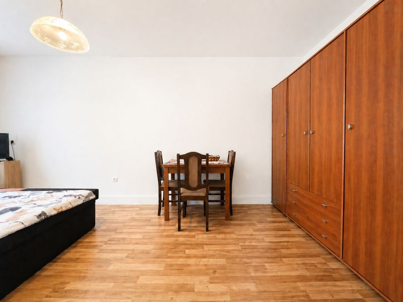 A room in a family house with a wooden floor decor, a bed, a wardrobe, and a dining table.