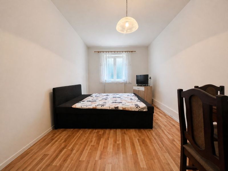 Bedroom in a family house with a bed, television, and wooden decor flooring.