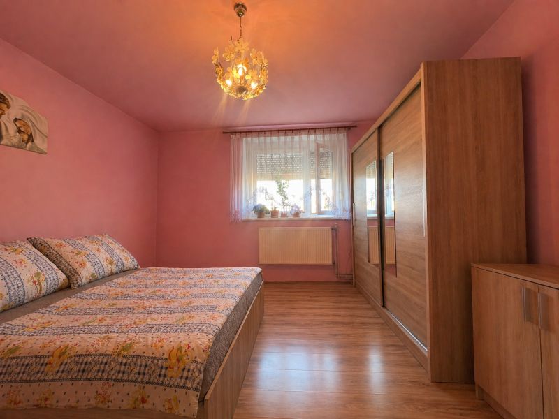 A bedroom with pink walls, a bed, and a wardrobe, with a wooden decor floor.