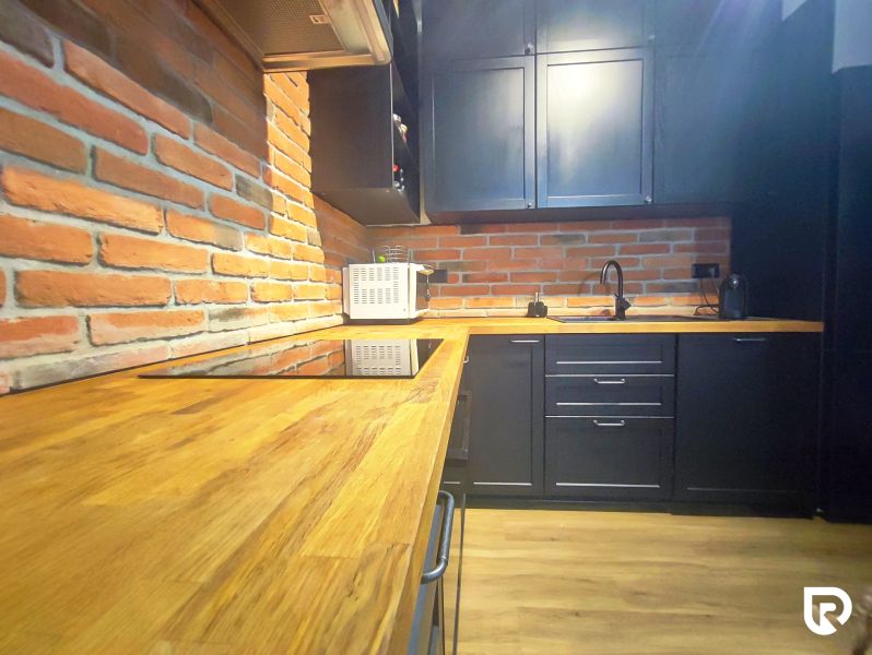 Kitchen in a 2-room apartment with a brick wall and a wooden decor floor.