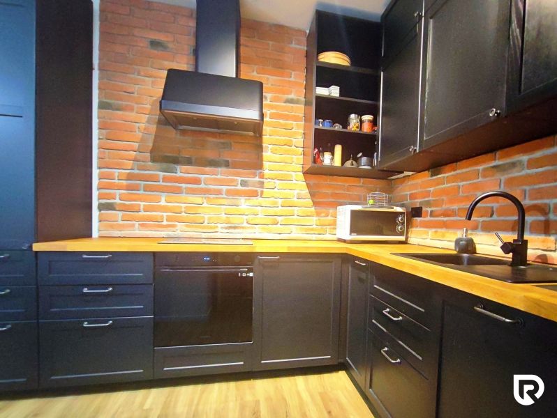 A kitchen in a 2-room apartment with a brick wall and a wooden decor floor.
