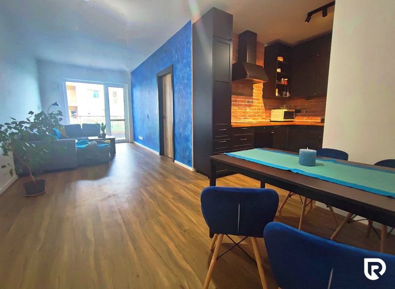 Living room with kitchen in a two-room apartment, with a wooden decor floor and colorful walls.