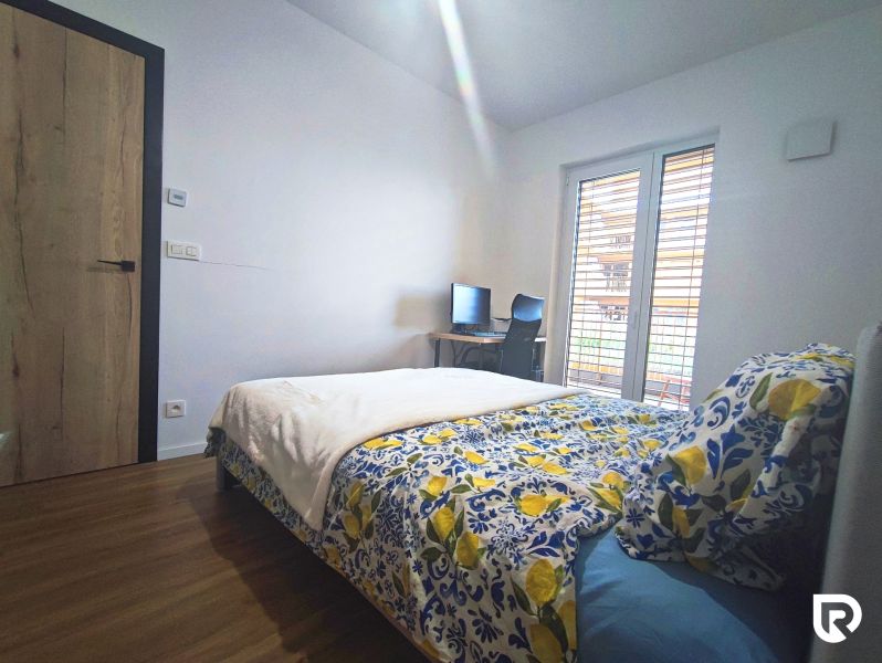 Bedroom in a 2-room apartment with a bed, wood-patterned floor, and a desk.