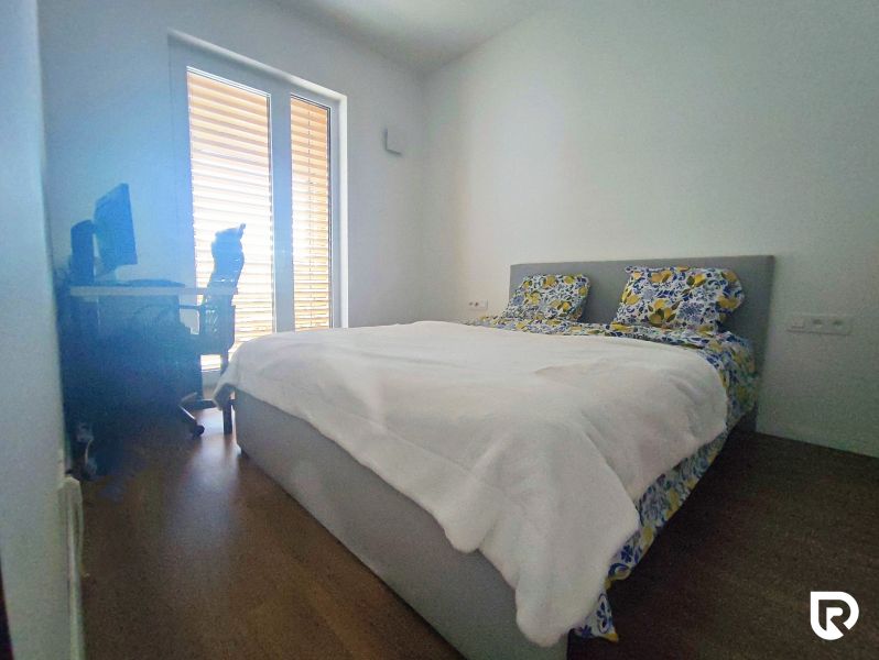 A bedroom in a two-room apartment with a wooden decor floor and a bed by the window.