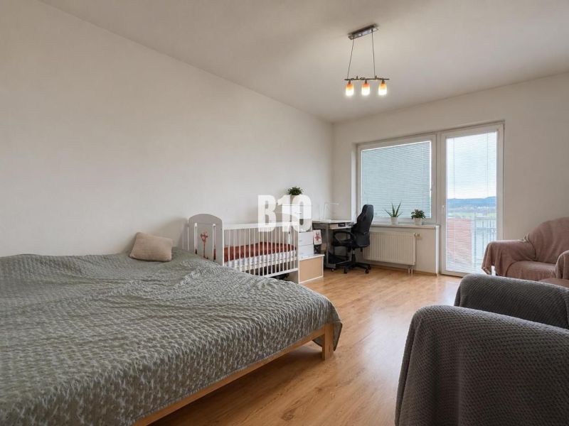 A bright room with a bed, a crib, and a wooden decor floor in a 2-room apartment.
