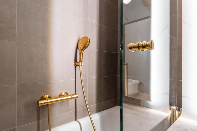 A bathroom with a bronze shower and neutral tiles in a 3-room apartment.