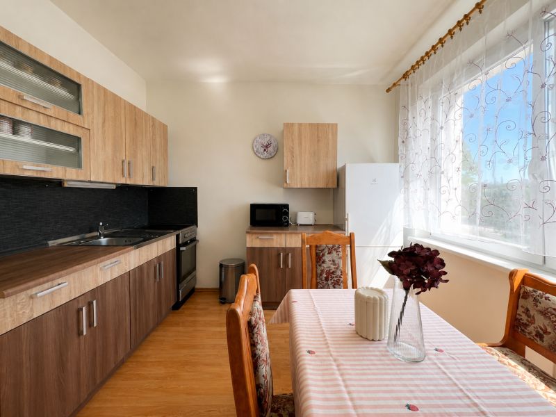 Kitchen corner with wooden cabinets in a studio apartment, light curtains, and a dining table.
