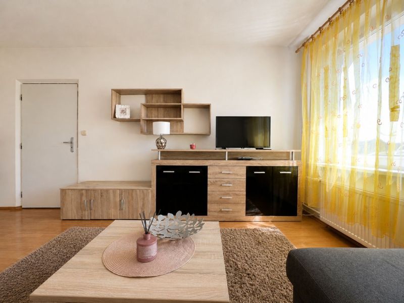 Living room in a studio apartment with wood-patterned flooring and yellow curtains.
