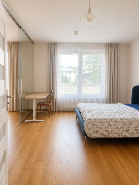 Bedroom in a 2-room apartment with a bed, table, curtains, and a floor with a wooden decor.