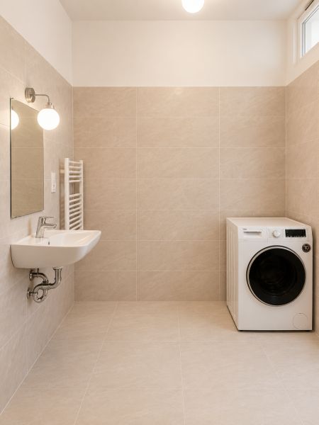 Bathroom in a 2-room apartment with a washing machine and a sink on light tiles.