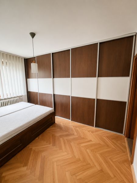 Bedroom with a sliding wardrobe, bed, and wooden decor flooring in a 2-room apartment.