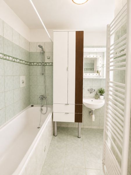 A bathroom in a 2-room apartment with green tiles and a practical bathtub.