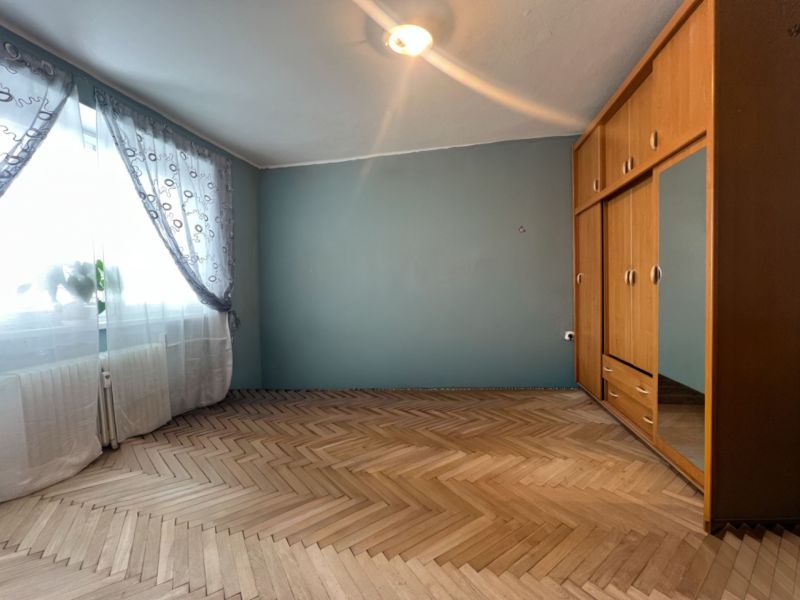 A room with a wooden decor floor, a wardrobe, and curtains in a two-room apartment.