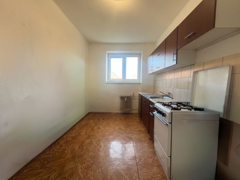 A kitchen in a 2-room apartment with a gas stove and a window, flooring with a wooden decor.