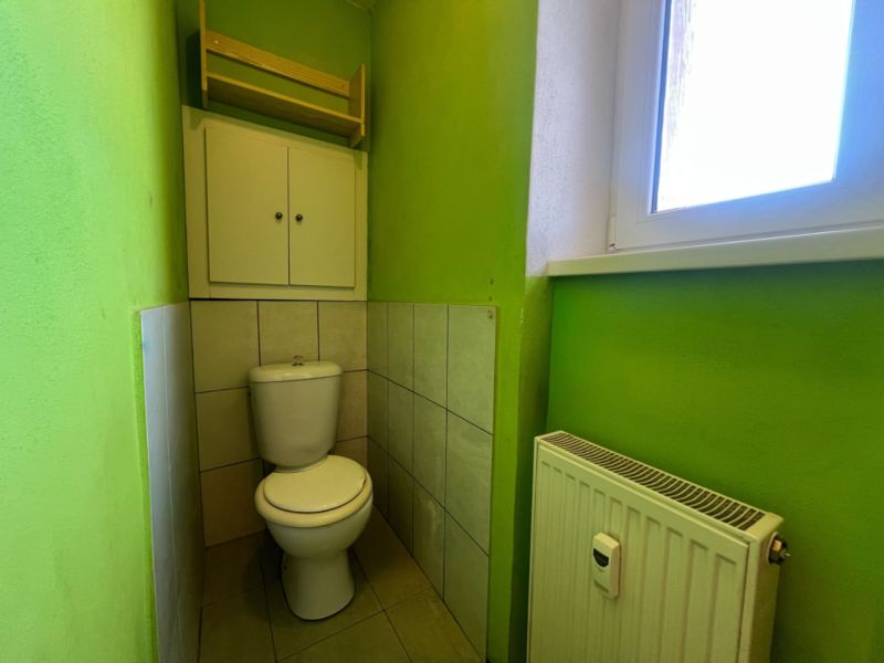 Green bathroom with a toilet, radiator, and window in a 2-room apartment.
